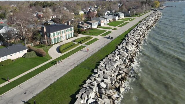 Motorcycles leading runners down residential road along the lake shoreline. Rocky riprap holding the lake water back. Waves of water against the rocks. Trees starting to bud out in the sunshine. 