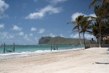 beach with palm trees and hammocks over the ocean waters with the porch of a tropical hut