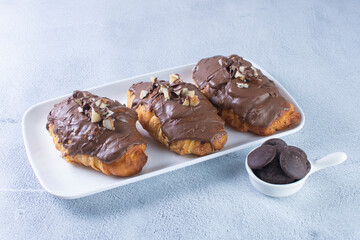 Chocolate croissant with walnut pieces, displayed on gray background