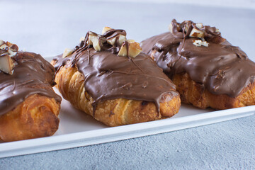 Chocolate croissant with walnut pieces, displayed on gray background