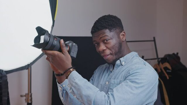 Excited middle-aged elegant african american man wearing a light blue shirt holding a professional camera pretending to take a picture. High quality 4k footage