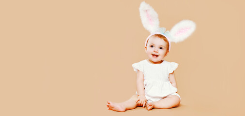 Portrait of cute baby with rabbit ears sitting on brown background