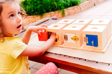 A girl manipulates sensory montessori material, wooden boxes to fit cubes. - obrazy, fototapety, plakaty