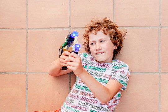 Blond boy playing with a fake toy gun, lying on the ground defending himself from an attack.
