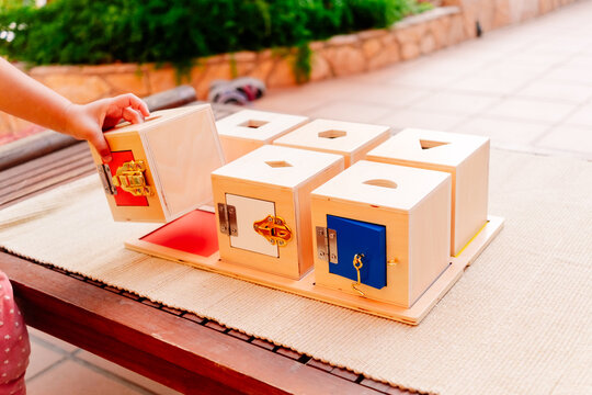 Little girl plays with a montessori educational material to open and close wooden boxes.