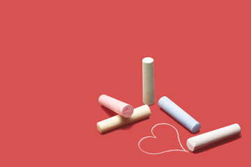 Chalks of various colors lying on a red background with a drawn heart.