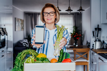 Woman holding a phone with blank white screen for copy space and fresh asparagus bunch. New Start of a healthy lifestyle, weight loss. Healthy food delivery, recipe box. Selective focus