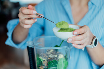 Close up woman adding wheat grass green powder during making smoothie on the kitchen. Superfood...