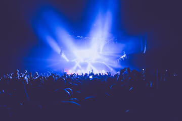 A crowded concert hall with scene stage lights in blue tones, rock show performance, with people...
