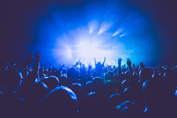 Fototapeta na wymiar A crowded concert hall with scene stage lights in blue tones, rock show performance, with people silhouette, on dance floor air during a concert festival