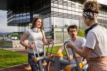 Group of friends man and women male and young adult people training at outdoor open gym in park in front of modern building real people sport and recreation exercise healthy lifestyle concept - obrazy, fototapety, plakaty