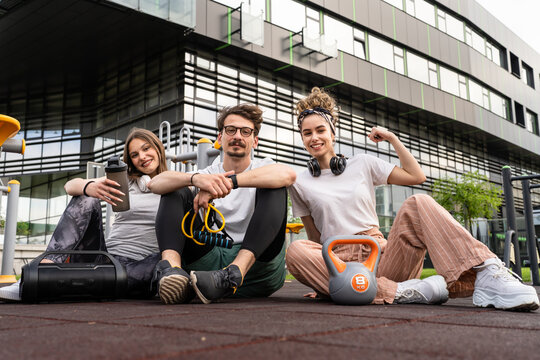 Group of people man and women male and female modern friends before or after training in open gym modern outdoor fitness park holding equipment kettlebell and resistance band front view sitting rest