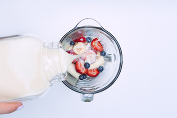 Making smoothie or milkshake in blender. Pouring milk in a blender with fruits. Vegan smoothie with...