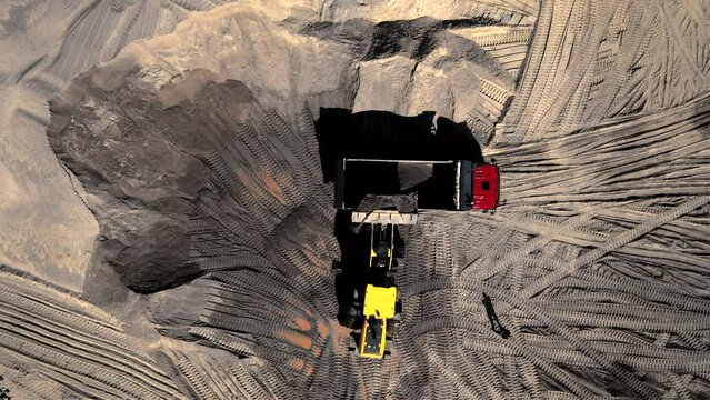 Front end loader on earthworks in quarry. Wheel loader load sand and gravel in dump truck in open pit. Heavy machinery in opencast. Mining truck transports crushed stones and sand from open-pit