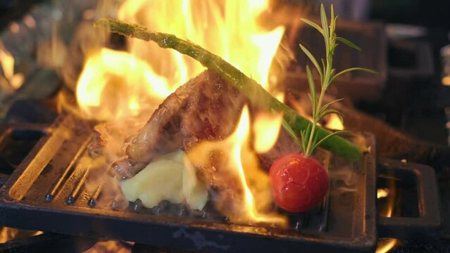 Chef in restaurant cooking flambe-style dish on frying pan. Steak with vegetables are fried with flame. Slow motion food footage. Open kitchen event. close up.4K