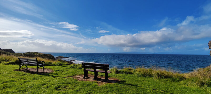 Beautiful landscape of a seaside with wooden benches and green grass in Scotland.