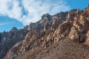 Scenic mountain landscape with sharp rocks under cirrus clouds in sunny day. Colorful scenery with gold sunlit sharp rocky mountains. High rocky mountains in golden sunlight under spindrift clouds.