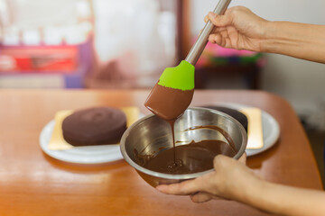 Woman mixing smooth delicious dark chocolate ganache with whisk in silver bowl.