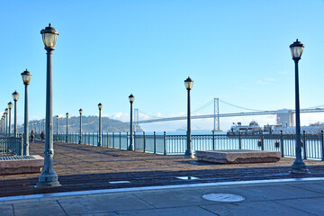 Historic old pier with lamp posts at the Embarcadero waterfront with Bay Bridge in the background in San Francisco, California