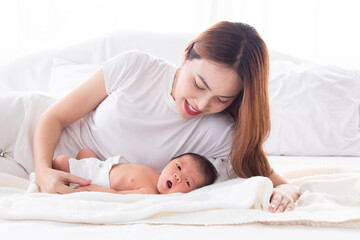 Beautiful asian mother and toddler lying in bedroom talking or singing together. Singlemom watching her son with love and tender. Mom playing with cute newborn baby and spend time together on bed.