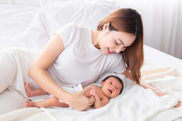 Fototapeta na wymiar Beautiful asian mother and toddler lying in bedroom talking or singing together. Singlemom watching her son with love and tender. Mom playing with cute newborn baby and spend time together on bed.