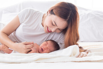 Beautiful young mother and toddler lying in bedroom talking or singing together. Singlemom playing with cute newborn baby and spend time together on bed, mom looking infant with love and tender.