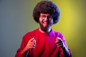Portrait of hipster man with Afro hairstyle pointing to camera, smiling, making happy choice, we...