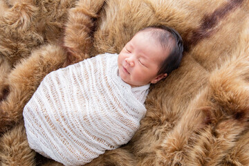 Asian little newborn baby deeply sleeping wrapped in thin white clothwith happy and safe on brown...