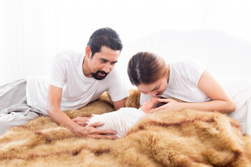 Asian young mother father and newborn lying on brown wool blanket  together. Mom and dad looking adorable infant with love and tender, Little baby deeply sleeping wrapped in thin white cloth.