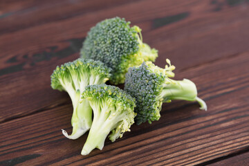 Break apart raw broccoli flowers on wood grain background