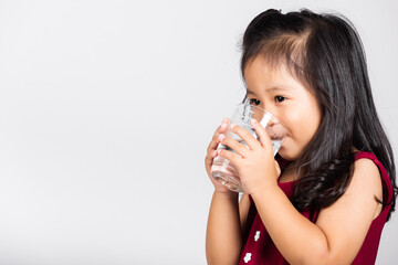 Little cute kid girl 3-4 years old smile drinking fresh water from glass in studio shot isolated on...