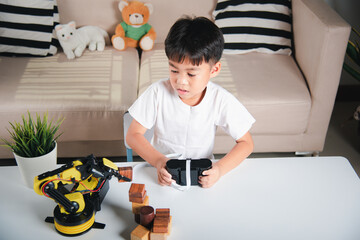 Happy Asian little kid boy using remote control playing robotic machine arm for pick up wood block,...