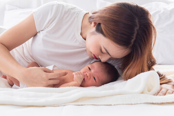 Obraz na płótnie Canvas Beautiful Asian mother kissing newborn while baby deeply sleeping with happiness. Little infant wrapped in thin white cloth with happy and safe. Young woman and toddler spend time together.