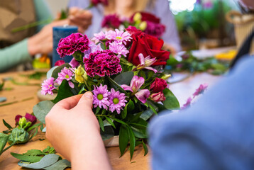 Florist at work: woman making fashion modern bouquet of different flowers on wooden background. Masterclass. Gift for bride on wedding, mother