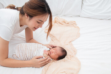 Obraz na płótnie Canvas Selective focus of Asian young mother swaddling baby on bed, Beautiful woman wrapping adorable infant in thin cloth. Cute newborn child taking nap after bath. Concept of baby care and family.