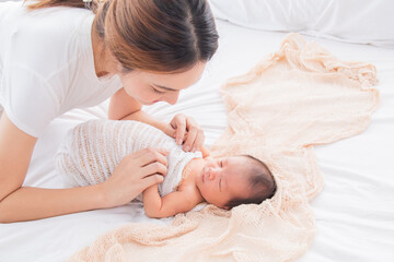 Obraz na płótnie Canvas Selective focus of Asian young mother swaddling baby on bed, Beautiful woman wrapping adorable infant in thin cloth. Cute newborn child taking nap after bath. Concept of baby care and family.
