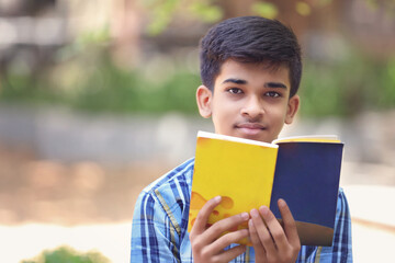 Indian teenage boy reading book in park