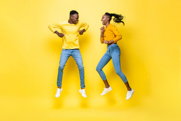 Fototapeta na wymiar Joyful smiling young African American couple jumping in yellow isolated studio background