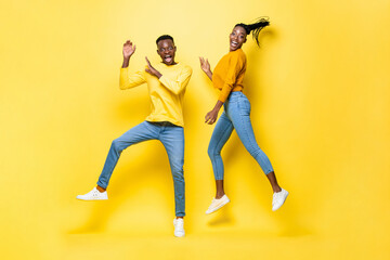 Fototapeta na wymiar Fun smiling young African American couple jumping in yellow isolated studio background