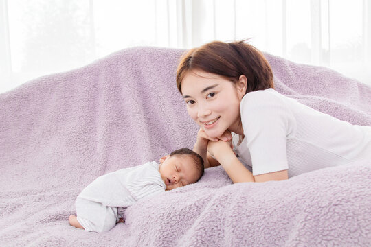 Beautiful asian mother take a photo with adorable newborn. Baby aged 0-1 months lying in bed. Concept of family happiness and loving parents with little children.