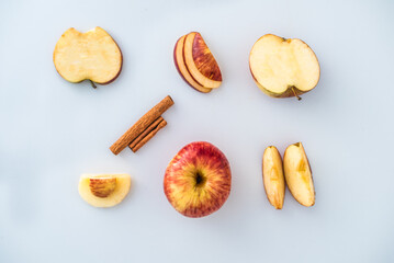 Top view of full and cut apple pieces and cinnamon on white background
