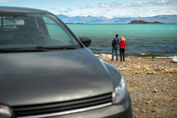 Adult couple looking at the sea with a black car parked on the beach on a windy day - Powered by Adobe