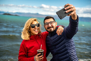 Shallow focus of a smiling Argentinian couple taking a selfie at the beach on a windy day