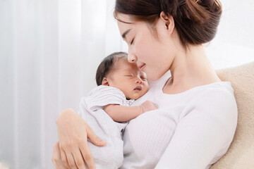 Asian mother holding her newborn in arm and sleeping together with love and care, adorable baby in mom arm sleeping with happy and safe, infant and mother concept.