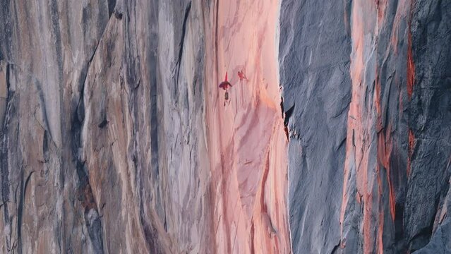 Mountain climber hanging on rope on El Capitan mountain in cinematic pink sunset reflecting on scenic sheer cliff rock. Yosemite park Firefall 6K RED camera USA extreme tourist climbing with efforts