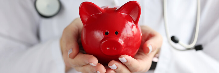Doctor holding red piggy bank in his hands closeup