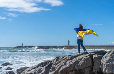 Young woman holding national a yellow and blue flag of Ukraine stands by the ocean. Concept of...
