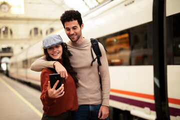 Fototapeta premium Beautiful couple at railway station waiting for the train. Young woman and man waiting to board a train.
