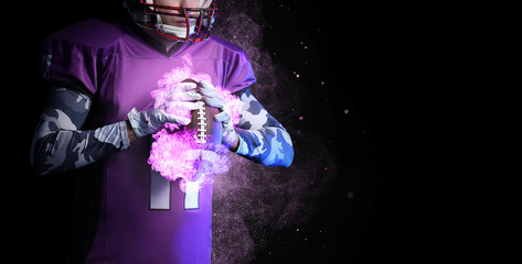 Sporty man with burning rugby ball on dark background