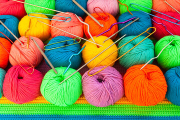 All for hand knitting. Knitted multi-colored handmade fabric with balls of multi-colored threads, pins and various knitting needles on it.